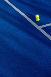 Two balls next to the lines of a paddle tennis court