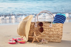 Summer beach bag with straw hat,towel,sunglasses and flip flops on sandy beach