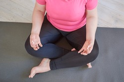 Top view of plus size woman with tracksuit meditating in lotus position while sitting on mat.
