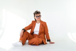 young emotional non binary person wearing orange color suit posing at studio