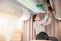 Flight attendant helps the passengers putting luggage into overhead locker on airplane.