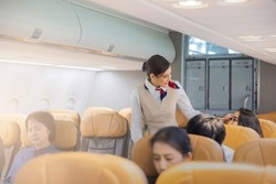 Beautiful female flight attendants checking the passengers on safety standard, seat belt, turn off electric devices, seat back and tray table in upright position before airplane take off and landing.