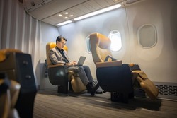 Flying at first class. Asian businessman working on laptop using wireless connection on board and thinking, analyzing data while sitting comfortable seat in airplane cabin business class. Copy space  