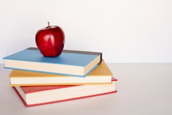 Pile stack of books with red apple on top sitting on a desk top, back to school concept, education teacher concept, horizontal shot copy text space, white background