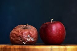 A Rotten and a Fresh Red Apple Next to Each Other. Good vs Bad. Antithesis Concept. Side View. Dark Background.