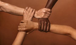 Four diverse women holding each others wrists in a circle. Top view of female hands linked in the lock against brown background.