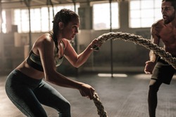Strong woman exercising with battle ropes at the gym with male trainer. Athlete doing battle rope workout at gym with instructor.