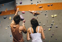 Rear view of male instructor giving instructions to a woman on wall climbing. Woman learning the art of rock climbing at an indoor climbing centre.