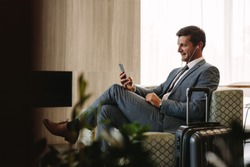 Business executive making a video call by mobile phone while waiting for his flight. Businessman at airport lounge doing a video conference call from his smart phone.