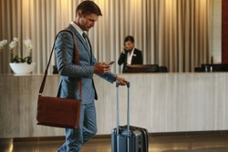Young businessman walking in hotel lobby and using mobile phone. Business traveler arriving at his hotel.