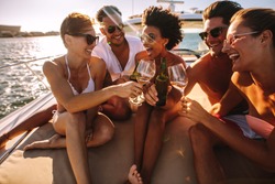 Multiracial group of people toasting drinks on the yacht deck and laughing. Cheerful men and woman partying on a boat.