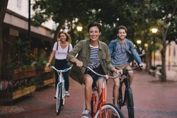 Three young people cycling down the street. Male and female friends on road with their bikes.