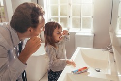 Father and daughter brushing teeth standing in bathroom. Man teaching his daughter how to brush teeth.