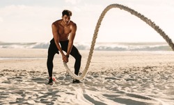 Man doing fitness workout at a beach on a sunny day. Bare chested man doing workout using a battle rope on the beach.