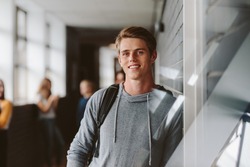 Portrait of teenage male student standing wall in corridor of a college. Caucasian male student in university campus.