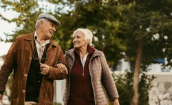Portrait of happy retired man and woman in warm clothing walking outdoors on street. Loving senior couple enjoy a walk together on a winter day.