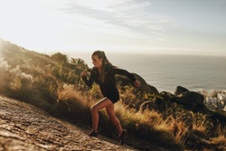 Fit young woman running up a rocky mountain trail. Woman trail runner training for uphill run.