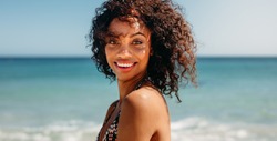 Side view of a smiling woman standing at the beach. Woman with curly hair standing on the beach with sea in the background.