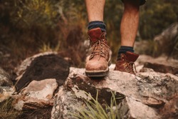 Closeup of male hikers shoes on rocky trail. Man walking through rugged path wearing trekking boots.