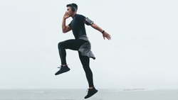 Sporty asian man doing intense exercises. Side view of fitness male exercising jump and lunge.