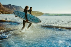 Two male surfers going for surfing in the sea. Two men carrying surfboards running in to the sea for surfing.