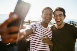 Two smiling young men taking selfie while standing by a car outdoors. Friends making a self portrait outdoors on a summer day.