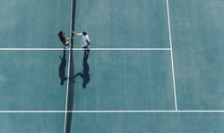 Aerial shot of professional tennis players handshakes at the net. Sportsmen shaking hands over the net on hard court.