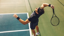 Top view of young tennis player jumping to hit the ball from the baseline of a hard court. Professional tennis player about to hit the ball for the serve.