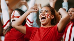 Female soccer fans of England watching and celebrating their team's victory. English female spectators enjoying after a win at stadium.