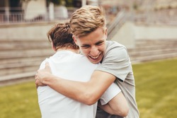 Two boys hugging each other in college campus. High school students smiling and giving each other a hug outdoors.