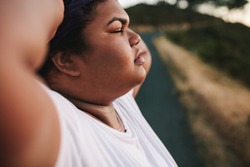 Closeup of woman standing outdoors with her hands behind her head. Oversized woman tired after exercising outdoors.