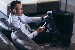 Mature businessman using a mobile phone while sitting in an airport cafe. Man waiting for his flight reading text message on his cell phone at first call lounge.