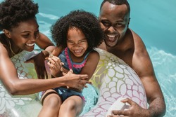 Man and woman playing with their daughter on inflatable ring in swimming pool. Family of three enjoying summer holidays in swimming pool.