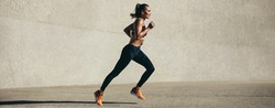 Healthy young woman running in morning. Fitness model exercising in morning outdoors. Panoramic side shot of fit woman.