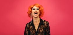 Portrait of drag queen laughing on red background. Gender fluid male dressed as female laughing.