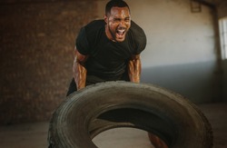 Male athlete flipping heavy tire inside an abandoned warehouse. Strong man flipping a tyre during an intense training session in a cross workout space.
