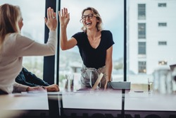 Businesswoman giving high five to colleague in meeting. Happy business professionals having meeting in office conference room.