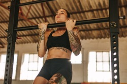 Female doing pull up workout in empty factory shade. Tattooed woman in sportswear exercising at an abandoned warehouse.