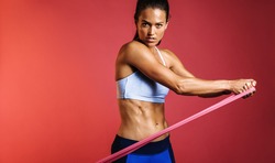 Portrait of fitness woman training using resistance bands. Female athlete working out with stretch bands on maroon background.