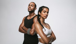 Close up of male and female athlete standing with arms crossed. Couple in fitness wear standing together at the gym.