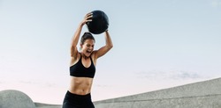 Sportswoman doing intense workout with medicine ball. Muscular woman screaming while exercising with medicine ball outdoors.