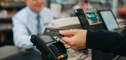 Close-up of a unrecognisable person using credit card to pay at grocery store. Customer making a payment for the purchase using his nfc card at supermarket.