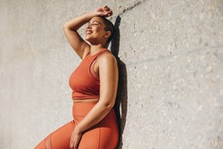 Woman with plus size body leaning to a wall and relaxing after workout session outdoors. Woman in sports clothing taking a break from exercise.