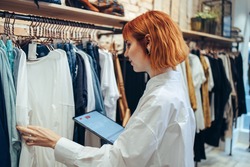 Woman taking inventory on digital tablet in clothing store. Woman manager in a fashion retail store using a tablet for working and checking the shop stock.