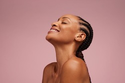 Close-up of a natural beauty smiling on pink background. Woman with beautiful skin having braided hair smiling and eyes closed.