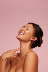 Woman with clean and clear skin smiling. Female model with eyes closed against pink background.