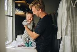 Father getting his son ready at home. Man at maternity leave taking care of his new born baby.