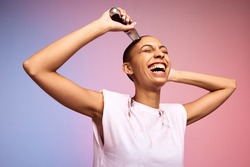 Smiling woman shaving her head. Bold and liberated female cutting her hair with an electric trimmer against multicolored background.