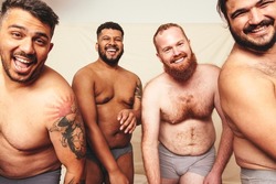 Having fun while shirtless. Three happy men smiling at the camera while wearing underwear in a studio. Body positive and self-confident men celebrating their natural bodies.