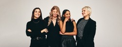 Happy group of women smiling in a studio. Four happy women looking cheerful while standing together against a studio background. Group of fashionable women standing in a studio.